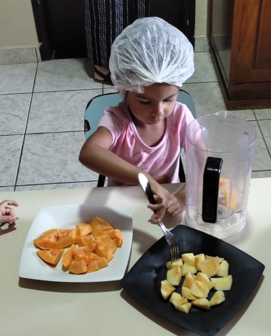 Menina de touca cortando frutas na aula de culinária