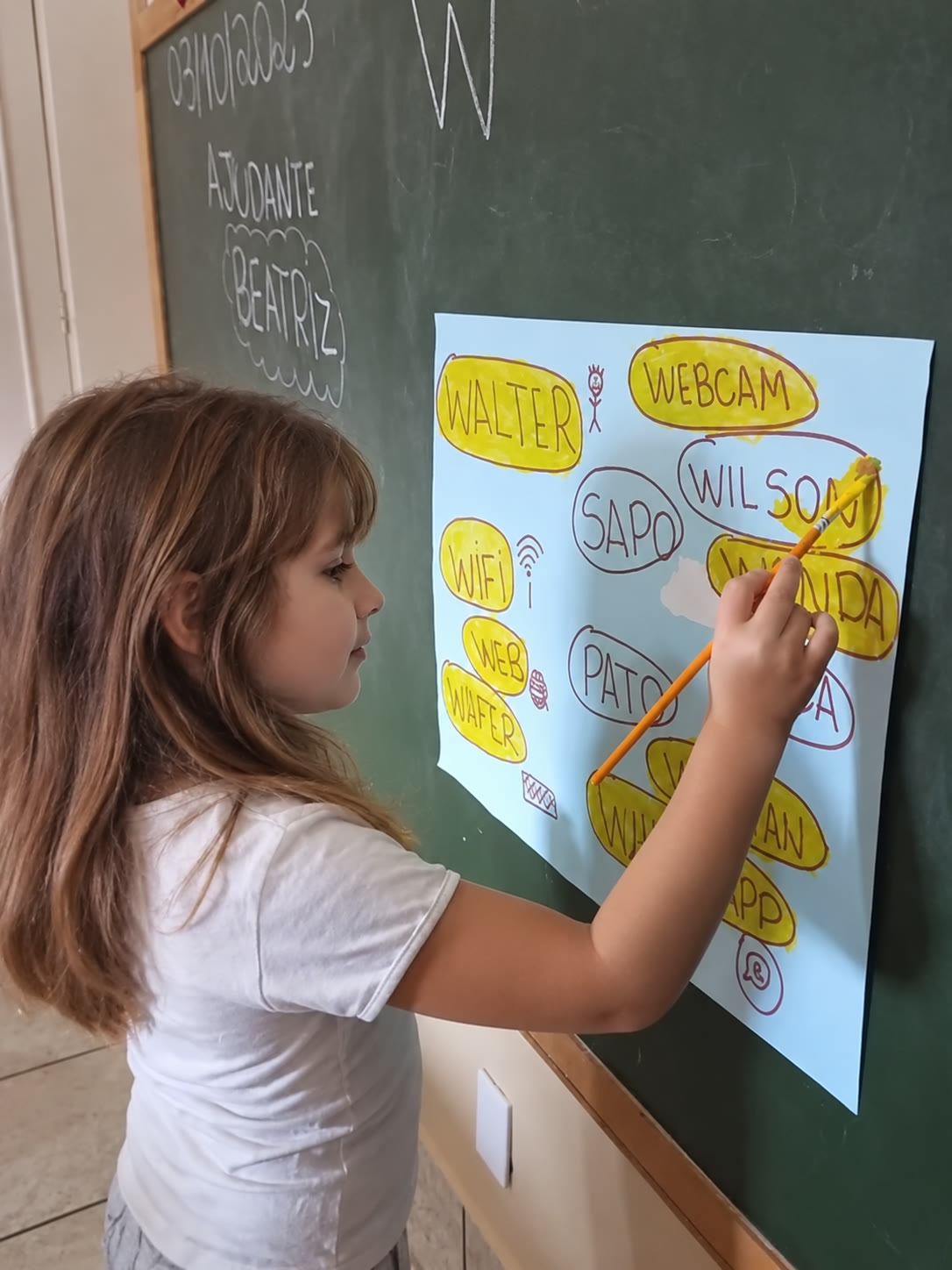 Menina circulando palavras num cartaz na lousa