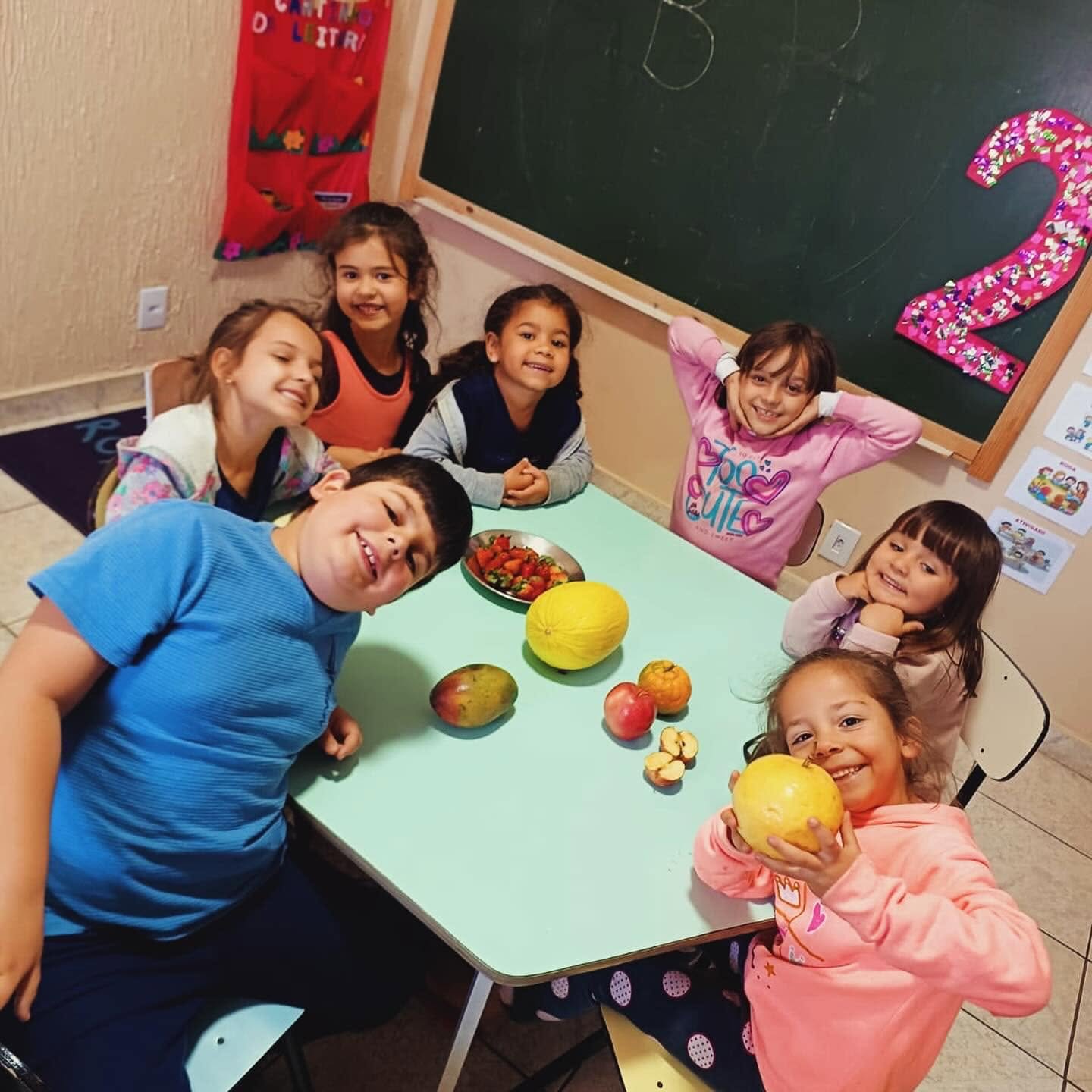 Crianças sorrindo em volta de uma mesa com frutas